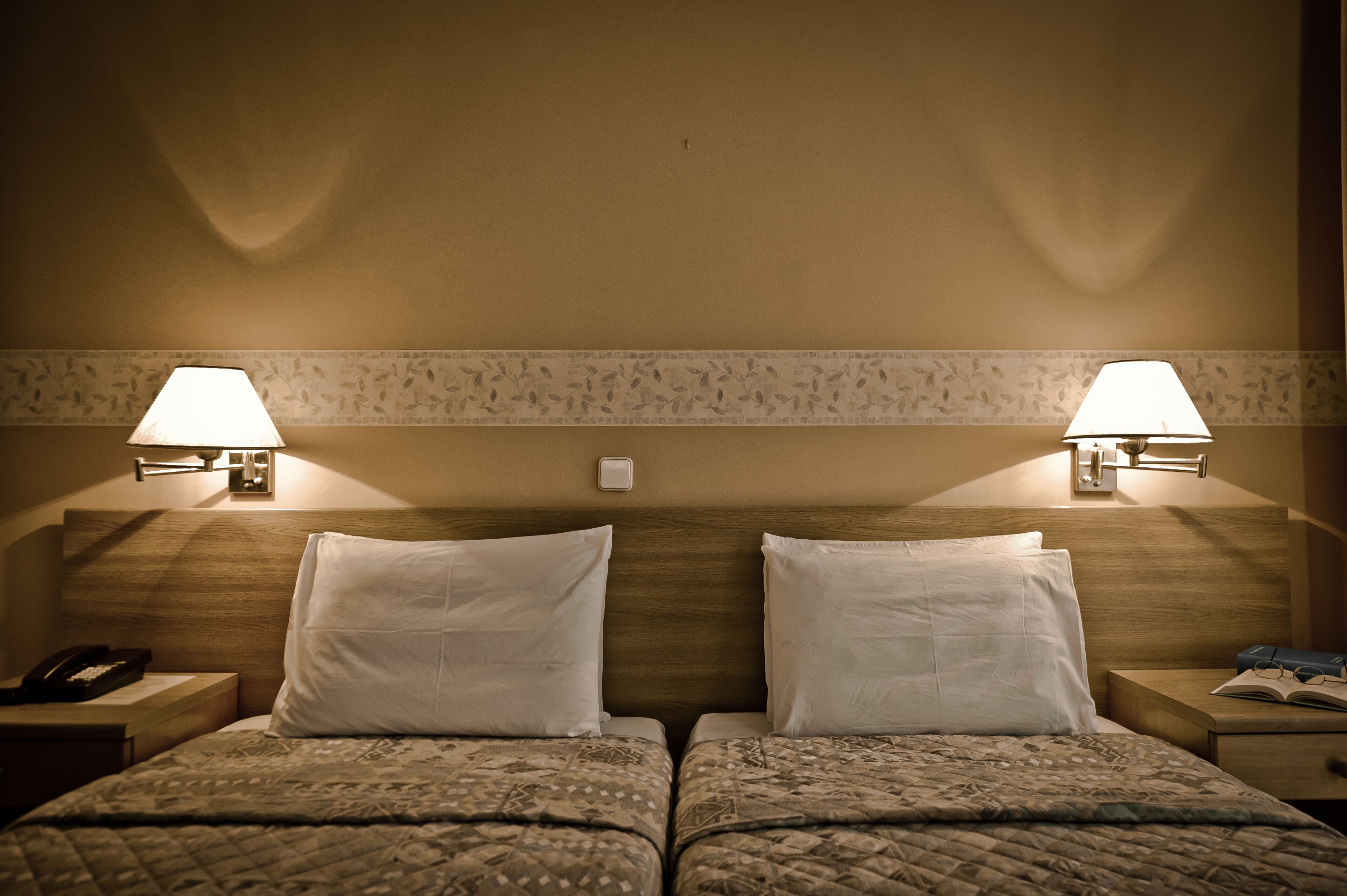 A hotel room with two beds, each with a nightstand, a lamp, and a telephone.