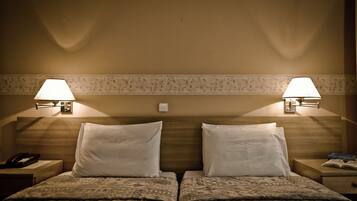 A hotel room with two beds, each with a nightstand, a lamp, and a telephone.