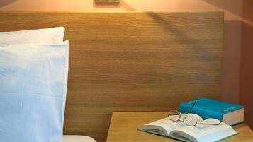 Een net opgemaakt bed met een kussen, een bedlampje, een boek en een bril op een nachtkastje.