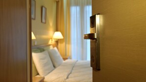 Ein Hotelzimmer mit Bett, Nachttisch, Lampe und einer Tür mit moderner Griffleiste.