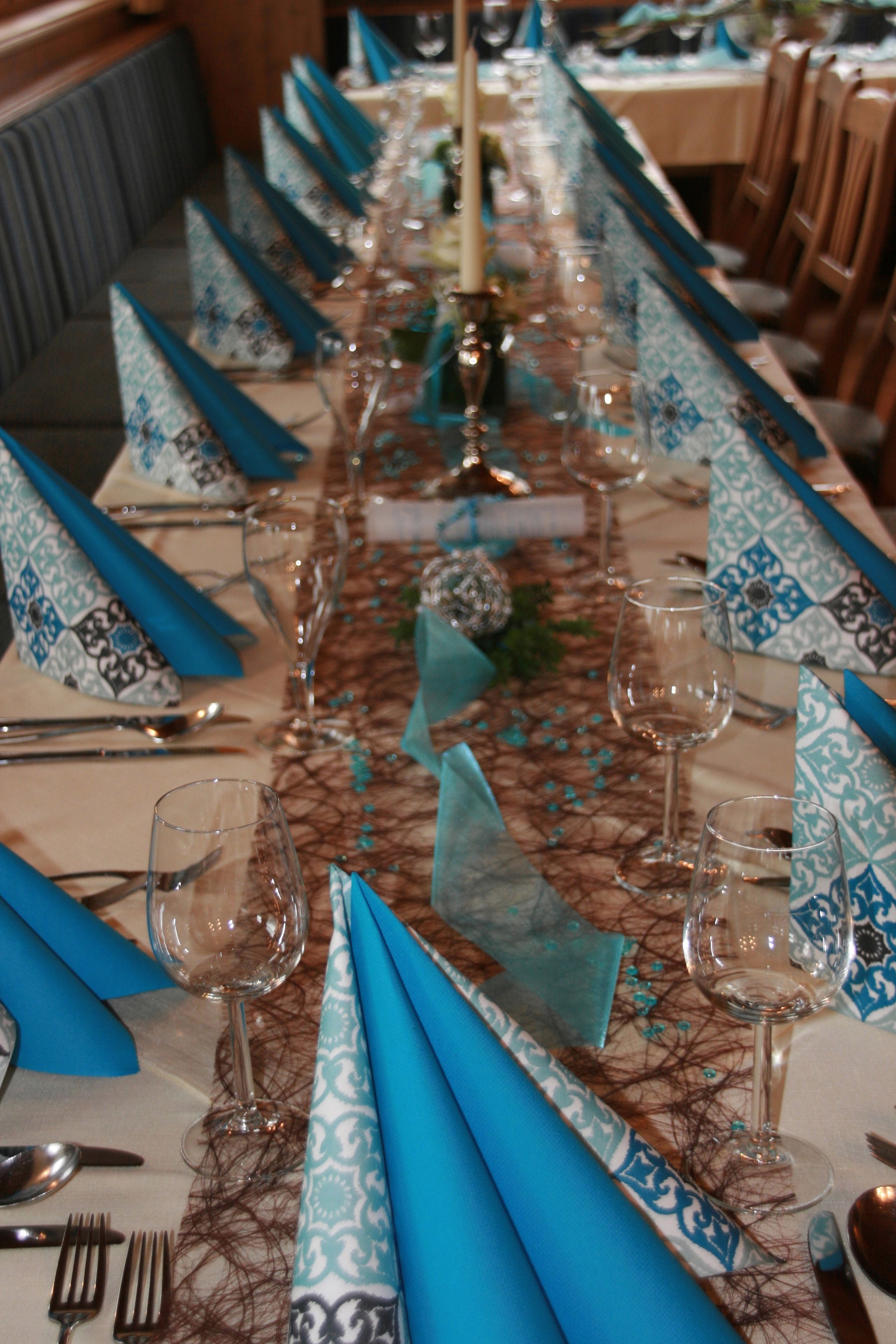 Ein langer Esstisch mit blauen Servietten und Gläsern, gedeckt für eine Mahlzeit.
