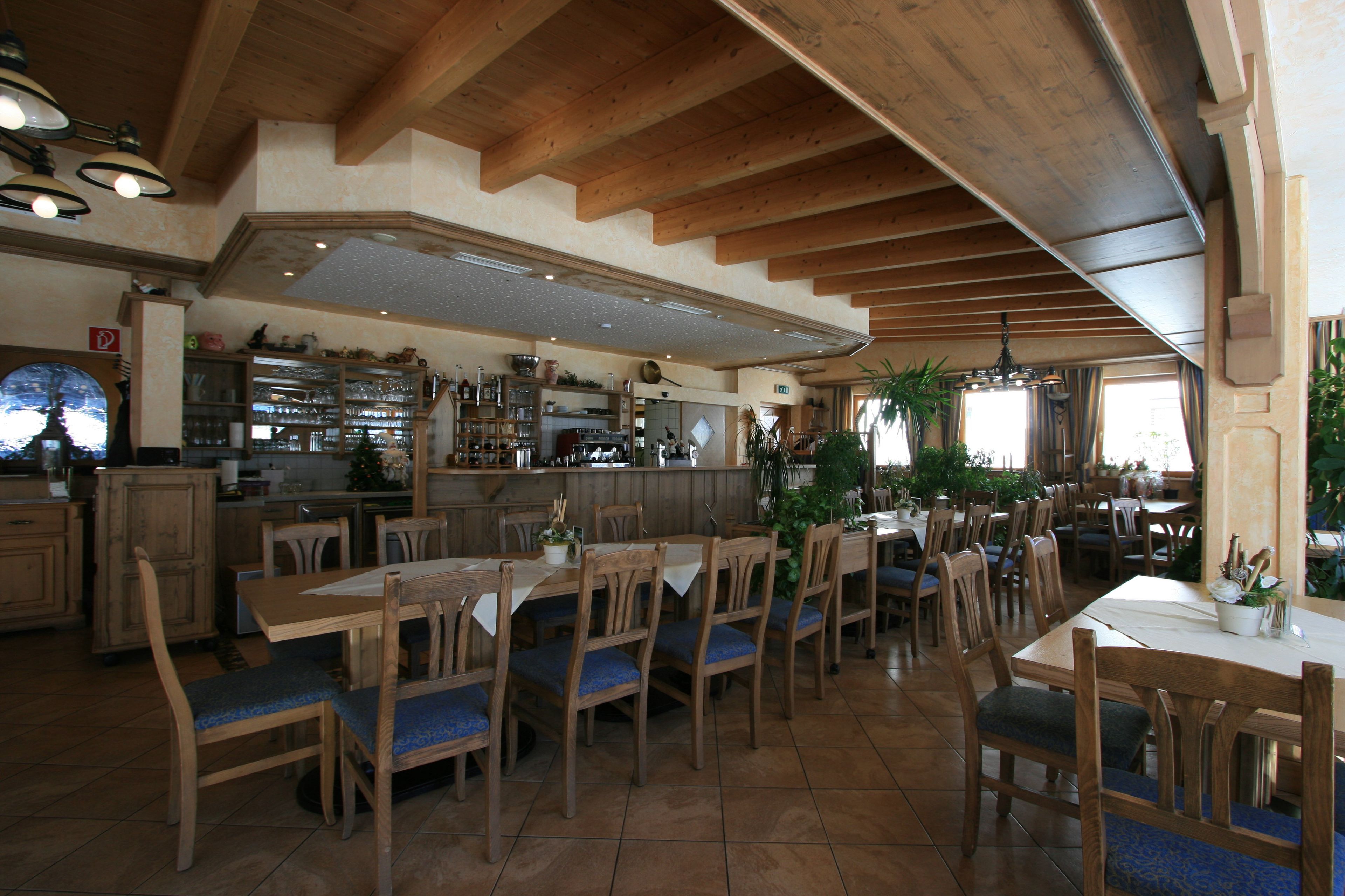Ein Restaurant mit Holztischen und -stühlen, einer Bar und Blick auf die Stadt durch große Fenster.