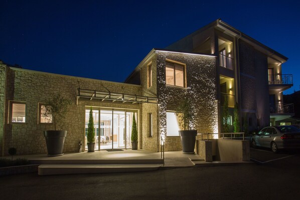 A modern building with a stone facade, large potted plants, and a well-lit entrance.