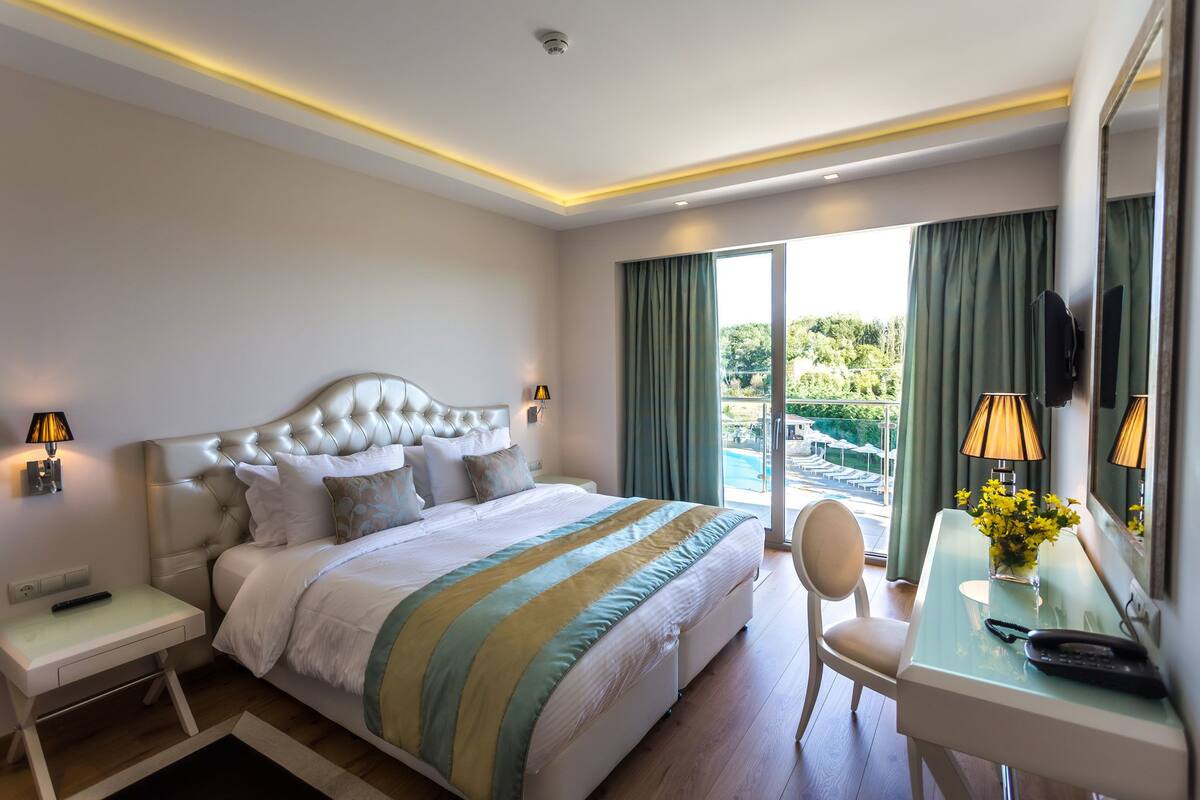 Habitación de hotel con una cama grande, un escritorio con silla, televisión y vistas al exterior.