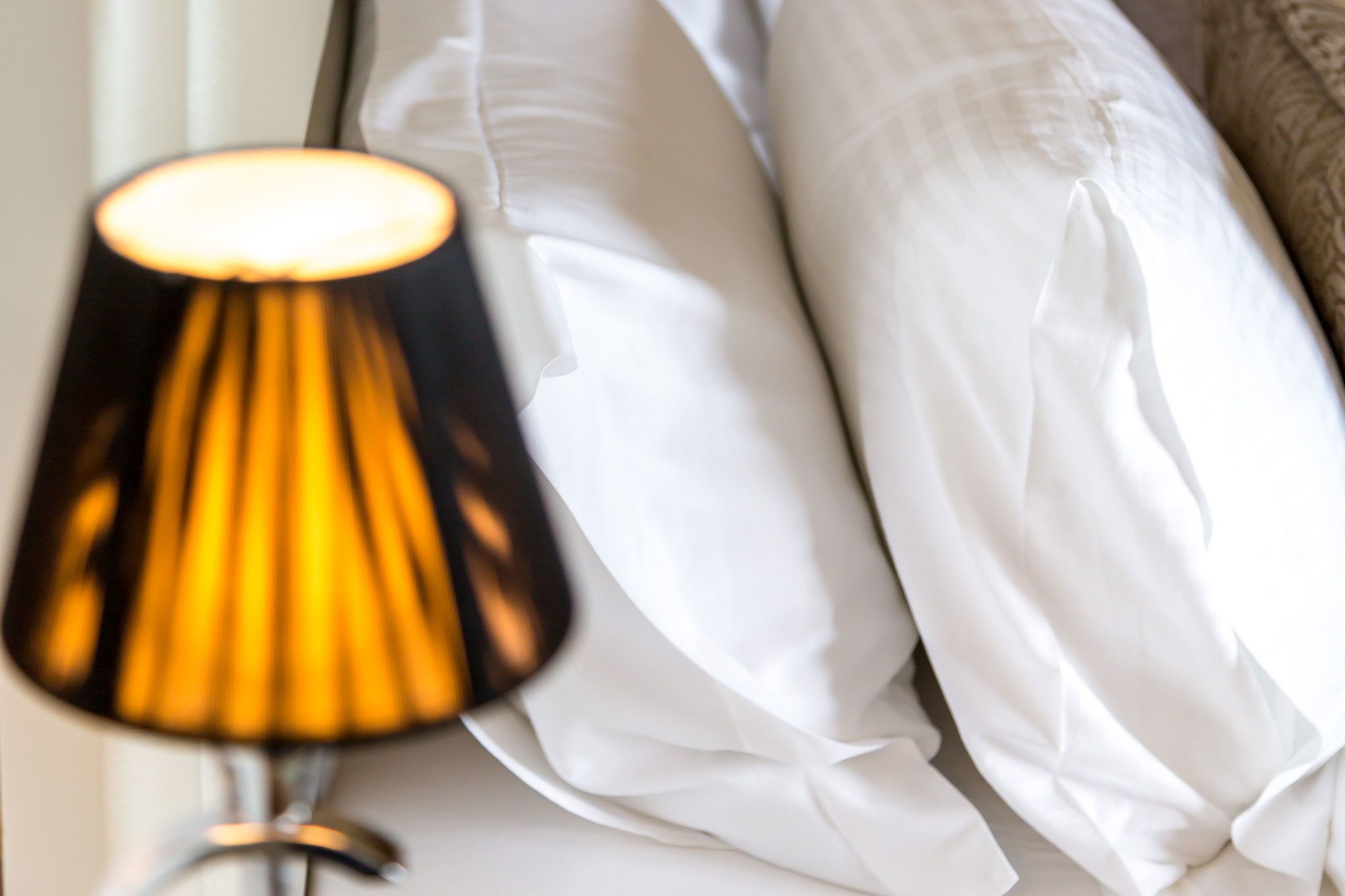 A bed with white pillows and a lamp with a black and yellow lampshade.