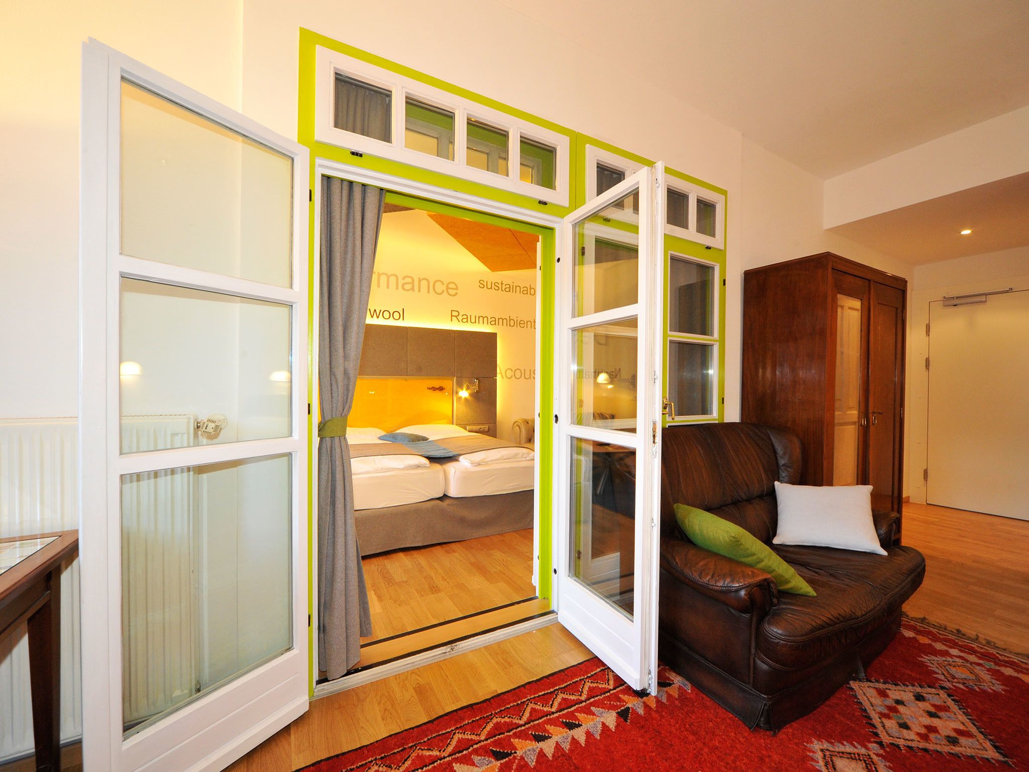 Una habitación de hotel con una cama, un sillón de cuero y un amplio ventanal con cortinas.