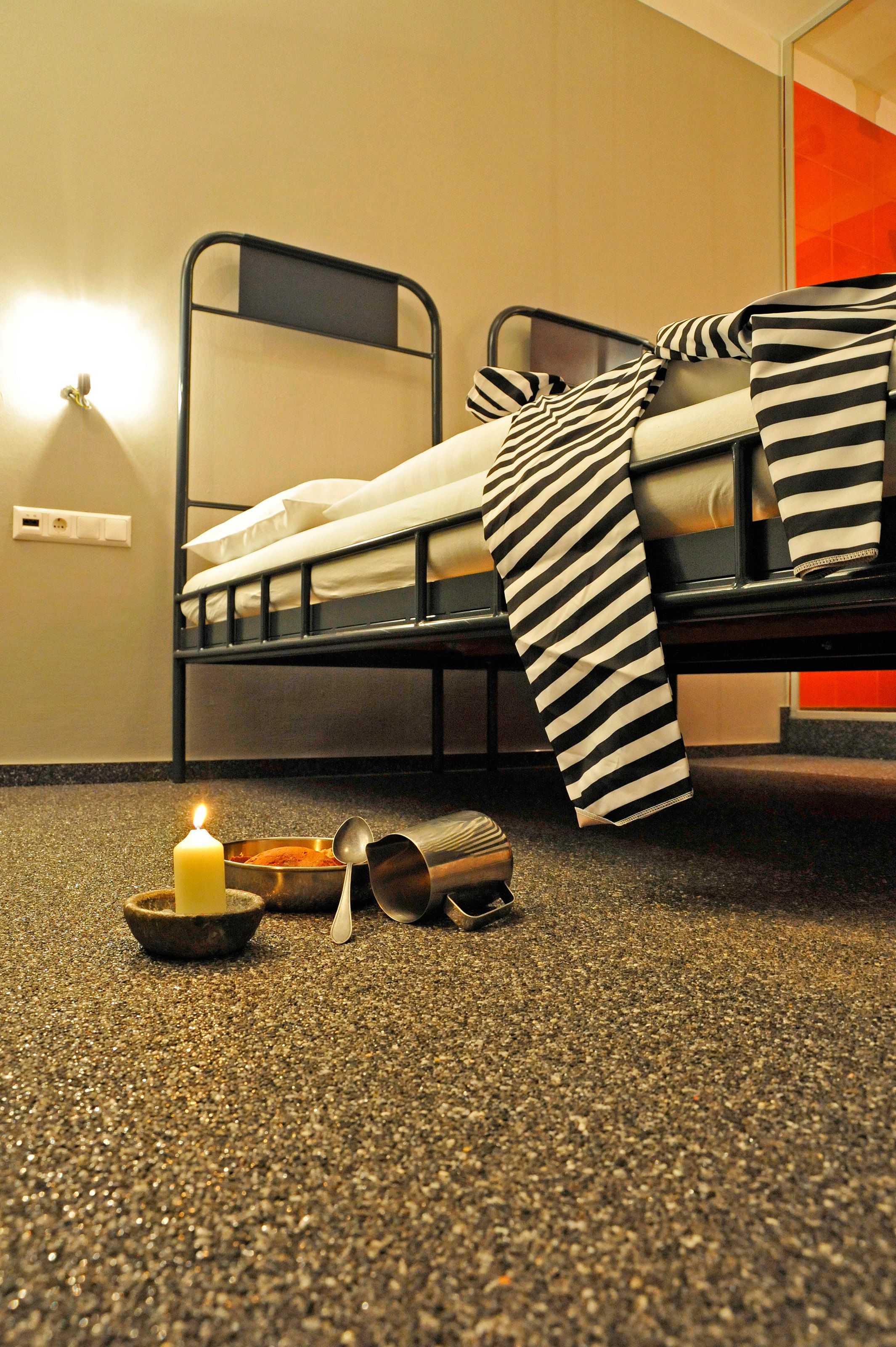 A bunk bed with striped bedding, a lit candle, a bowl, and a spoon on a speckled carpet.