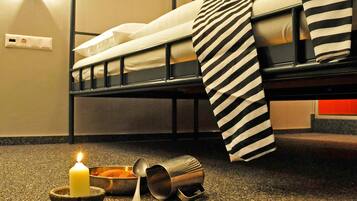 A bunk bed with striped bedding, a lit candle, a bowl, and a spoon on a speckled carpet.