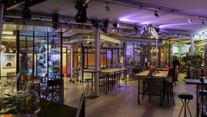 Un comedor interior con mesas y sillas, una zona de cocina al fondo, y un diseño moderno de estilo industrial.