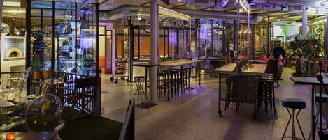 An indoor dining area with tables and chairs, a kitchen area in the background, and a modern industrial design.