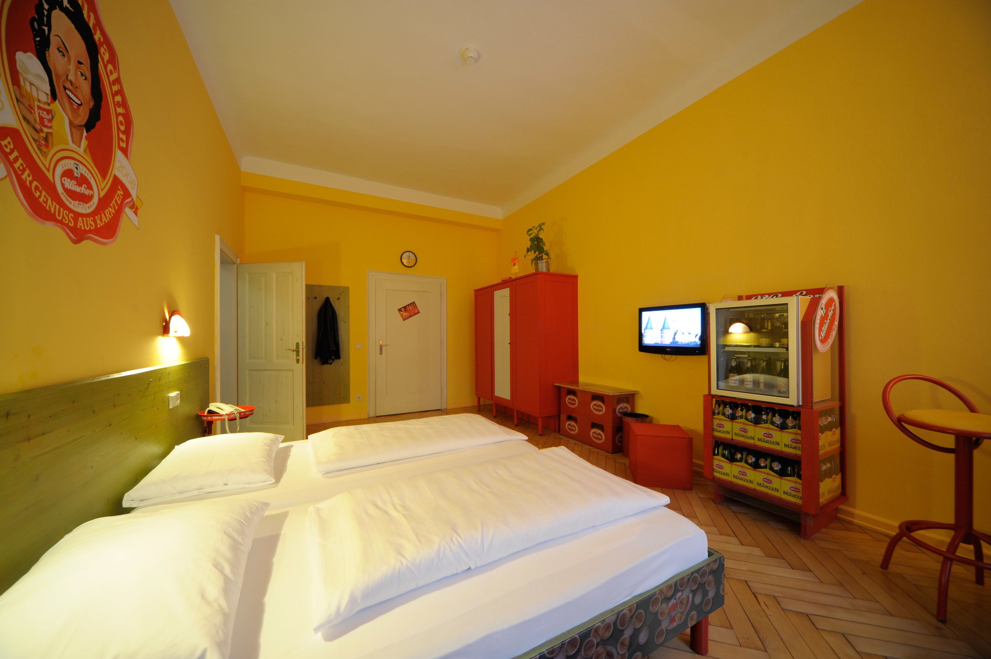 Una camera d'albergo con due letti, un minibar, una televisione e una sedia rossa.