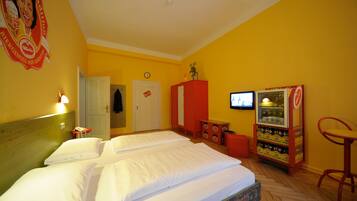 A hotel room with two beds, a minibar, a television, and a red chair.