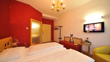 Habitación de hotel con una cama grande, un televisor montado en la pared, una pared roja y un sillón amarillo.