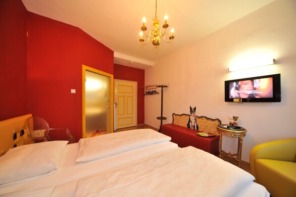 Habitación de hotel con una cama grande, un televisor montado en la pared, una pared roja y un sillón amarillo.