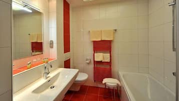 Un baño con lavamanos, inodoro y bañera. Hay un espejo sobre el lavamanos y un perchero con toallas.