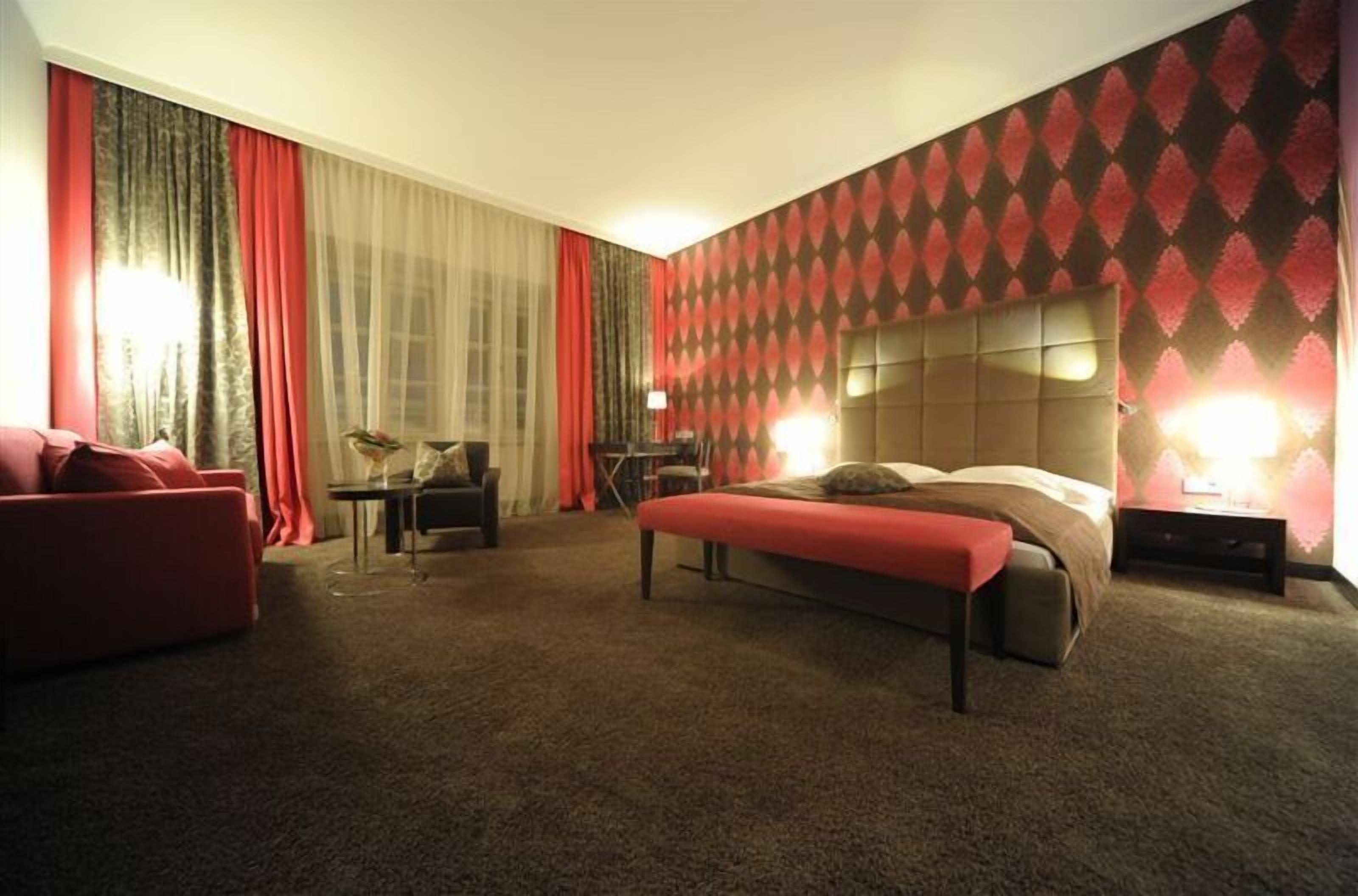Habitación de hotel con una cama grande, un sofá rojo, una mesita y una lámpara.