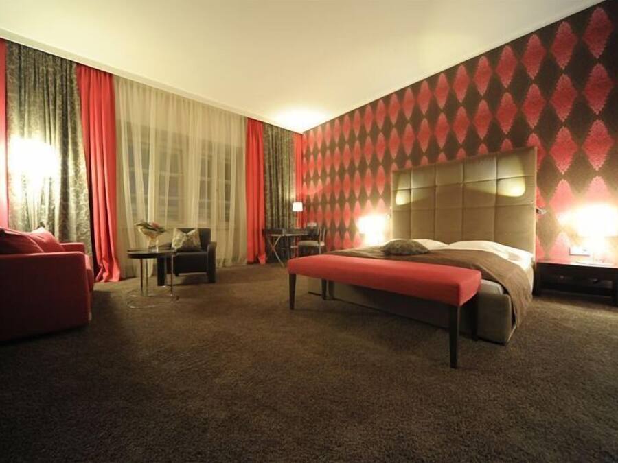 Habitación de hotel con una cama grande, un sofá rojo, una mesita y una lámpara.