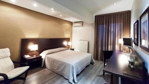 A hotel room with a bed, bedside tables, a chair, a desk with a lamp, and a window with curtains. - Aliakmon Hotel (Kozani)