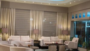A spacious lobby with a modern design, featuring a seating area with sofas and armchairs, a large window with curtains, and a decorative ceiling. - Aliakmon Hotel (Kozani)