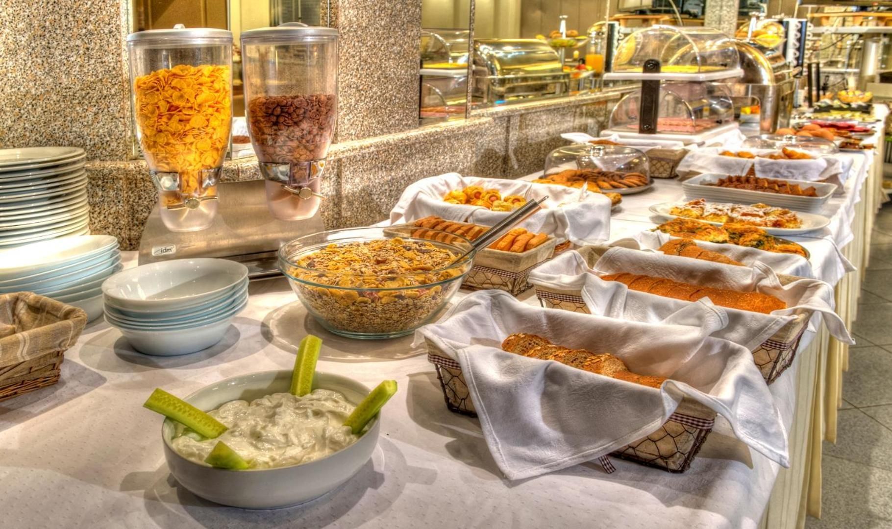 A buffet with various food items, including cereal, fruits, and a bowl of dip with celery sticks.