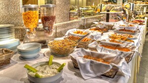 A buffet with various food items, including cereal, fruits, and a bowl of dip with celery sticks. - Aliakmon Hotel (Kozani)