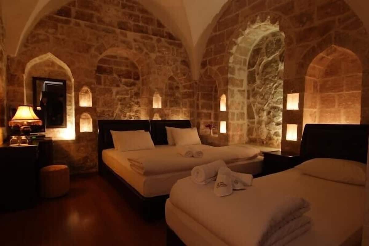 Una habitación con dos camas, paredes de piedra y arcos.