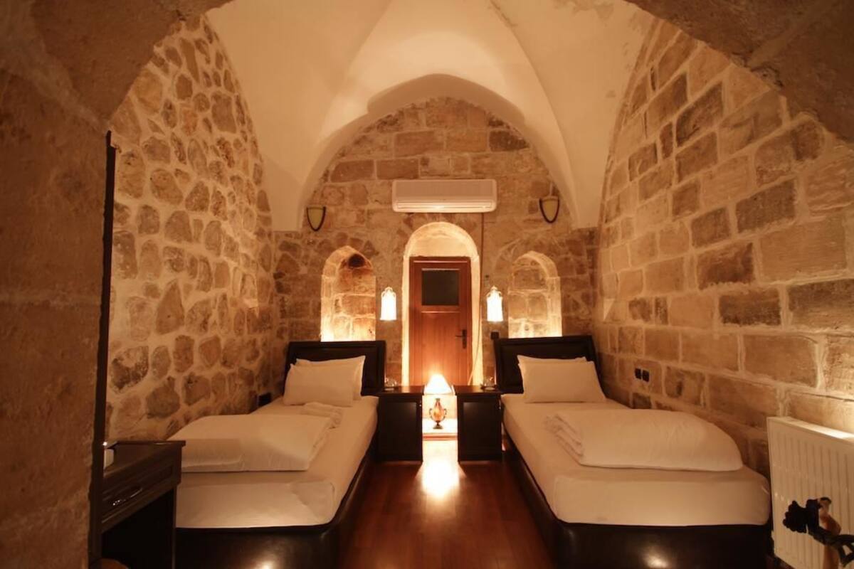 Una habitación con dos camas, paredes de piedra, techo abovedado y un acceso central.