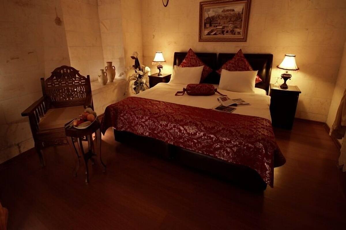 Una habitación de hotel con una cama grande, dos mesitas de noche con lámparas, una silla de madera y un cuadro en la pared.