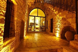 A stone-walled corridor with a large arched doorway leading to a well-lit interior space. - Zinciriye Hotel - Special Class (Mardin)