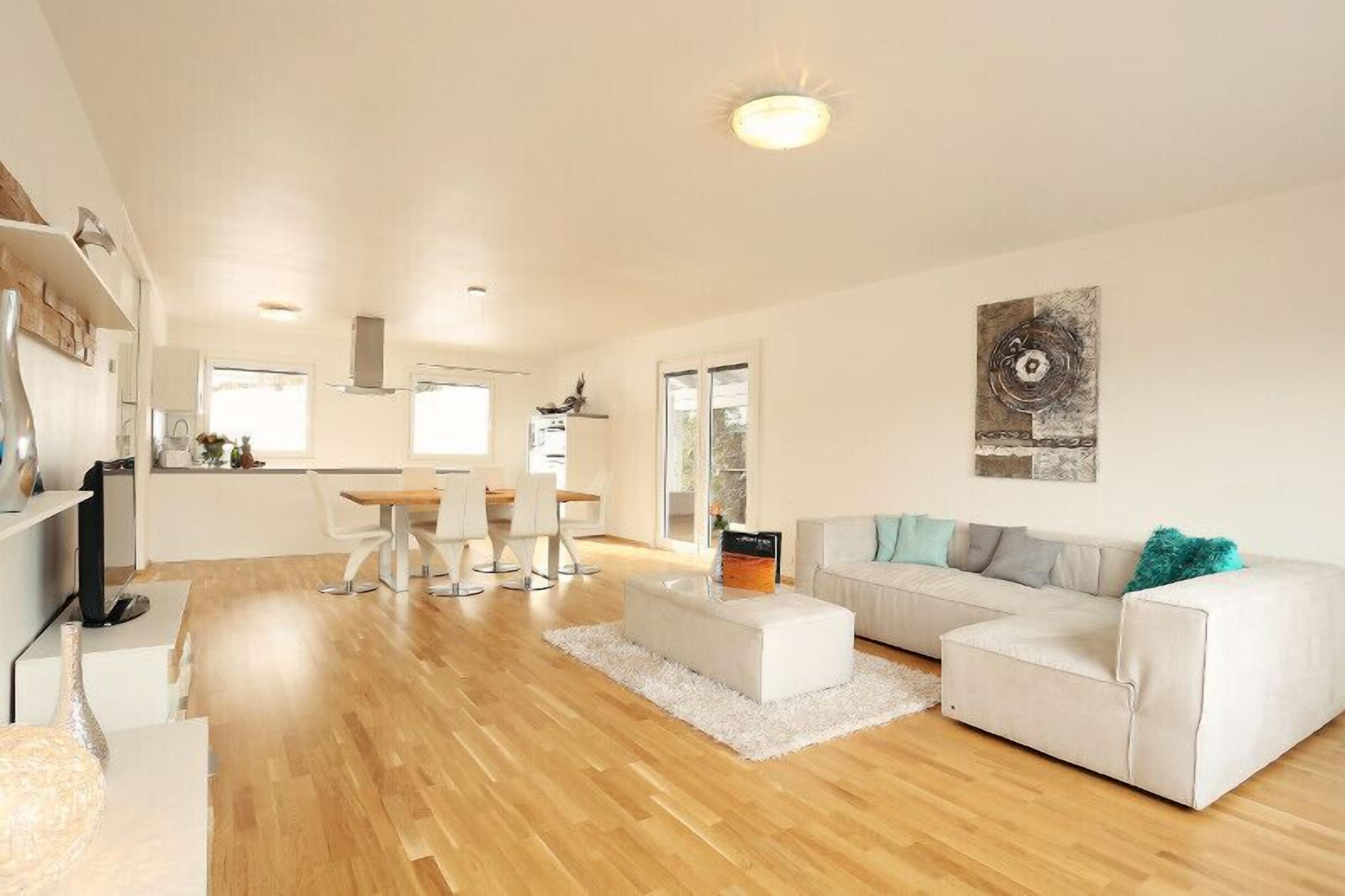 A spacious living area with a white sofa, a coffee table, and a dining area with chairs and a table.