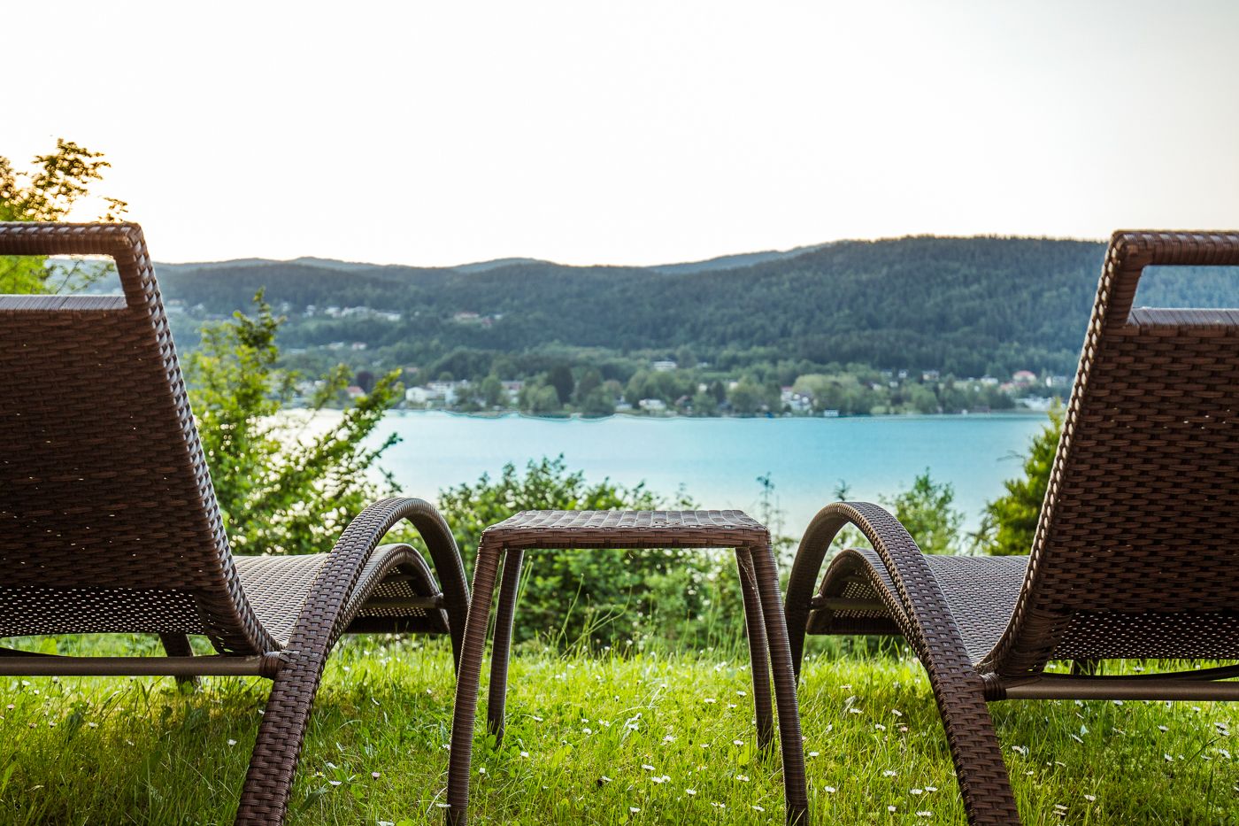 Two wicker chairs facing a lake with a view of a forested hillside.