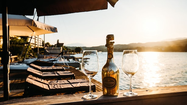 A waterfront view with a bottle of Prosecco and two glasses on a wooden railing.