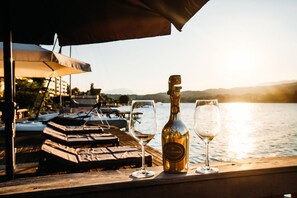 A waterfront view with a bottle of Prosecco and two glasses on a wooden railing. - Seevillen Excelsior (Velden am Wörther See)
