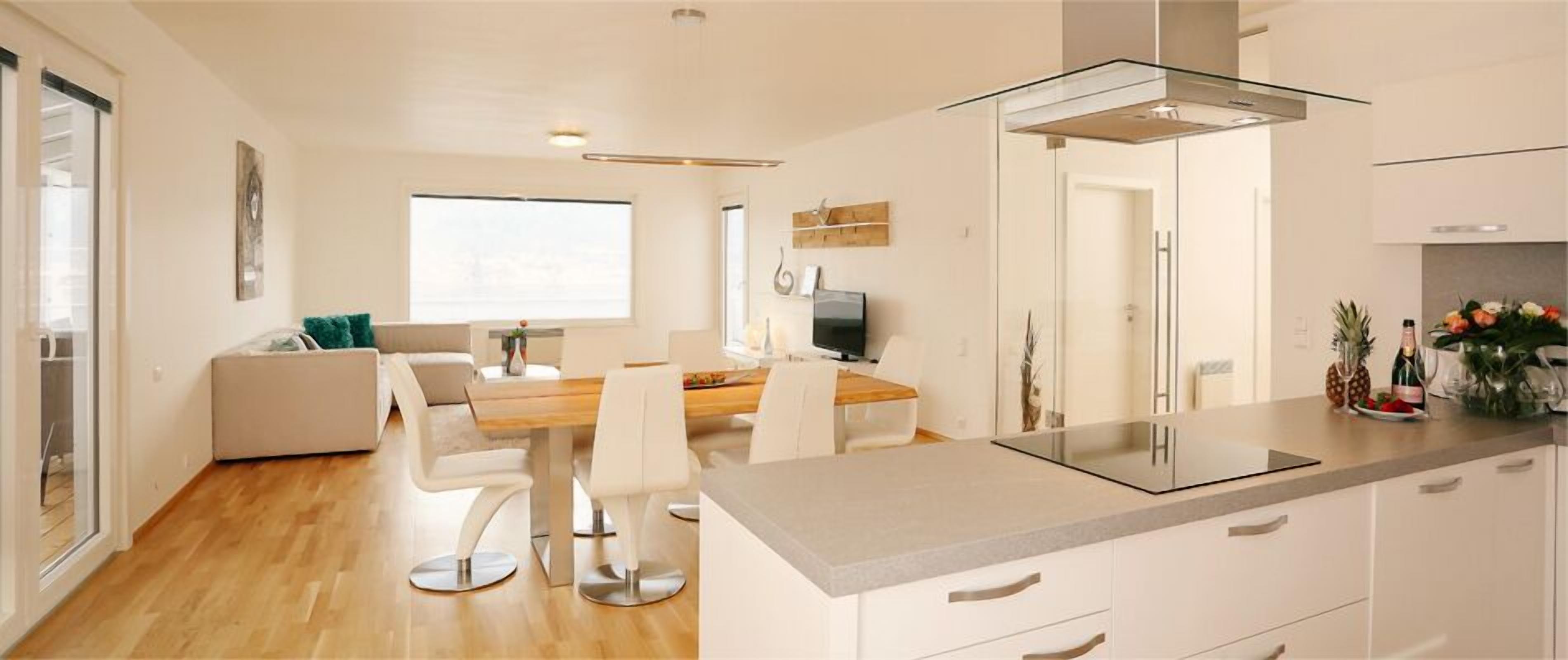 Een moderne keuken met een glazen kookplaat, witte kasten en een eethoek met een houten tafel en stoelen.