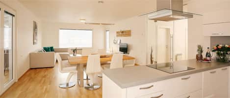 Een moderne keuken met een glazen kookplaat, witte kasten en een eethoek met een houten tafel en stoelen.