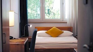 A hotel room with a bed, a desk, a lamp, and a window with a view of trees. - Na Skarpie (Chojnice)