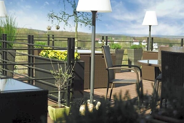 An outdoor patio with wicker furniture, potted plants, and a view of the landscape.