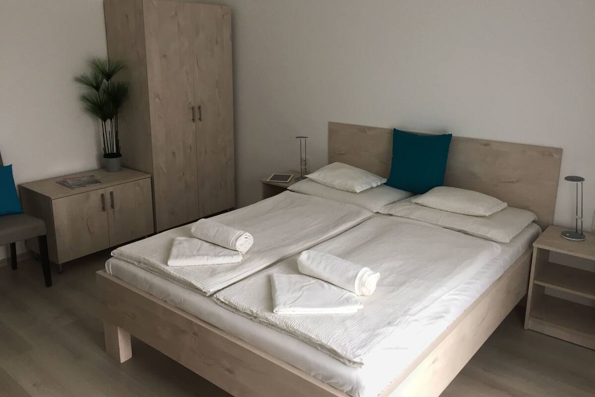A neatly made bed with towels, a wooden wardrobe, a bedside table, and a small plant.