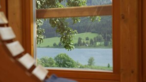 Une fenêtre à cadre en bois donnant sur un lac et des collines verdoyantes.