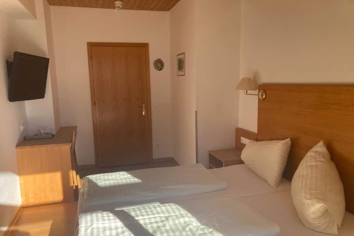 Habitación de hotel con cama de madera, mesita de noche, lámpara, televisor montado en la pared y una puerta.
