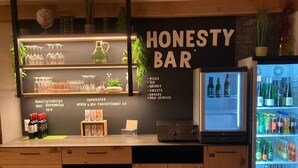 Un espace bar avec un menu proposant des pizzas, des glaçons, des boissons, des desserts, des en-cas et un service en libre-service. On y trouve des bouteilles de vin, des verres et un réfrigérateur rempli de boissons.