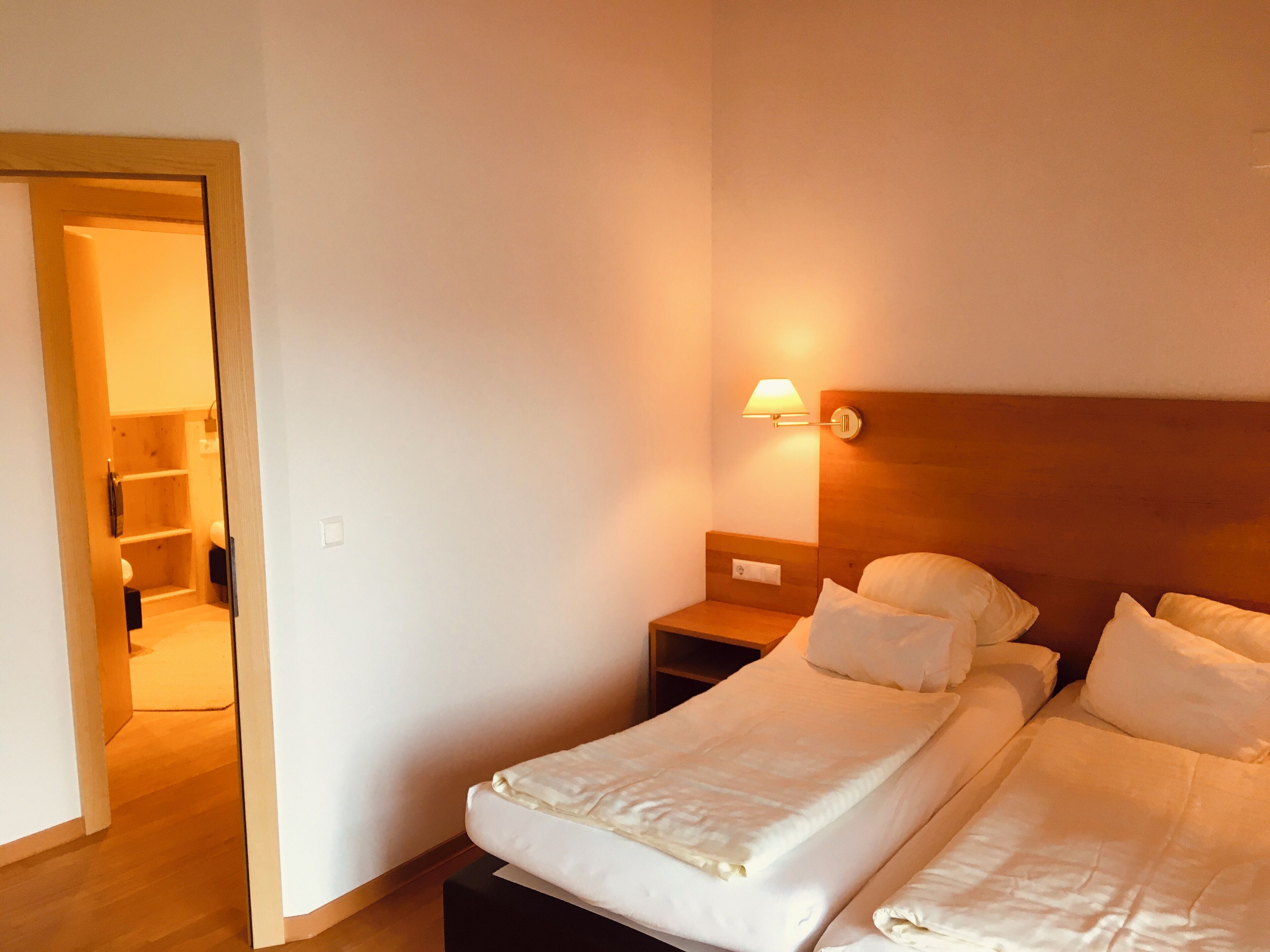 Een hotelkamer met een houten hoofdeinde, een nachtkastje met een lamp, en een bed met wit beddengoed.
