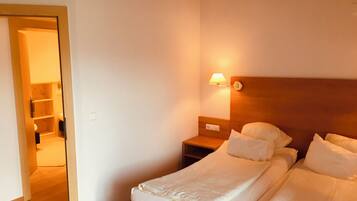Een hotelkamer met een houten hoofdeinde, een nachtkastje met een lamp, en een bed met wit beddengoed.