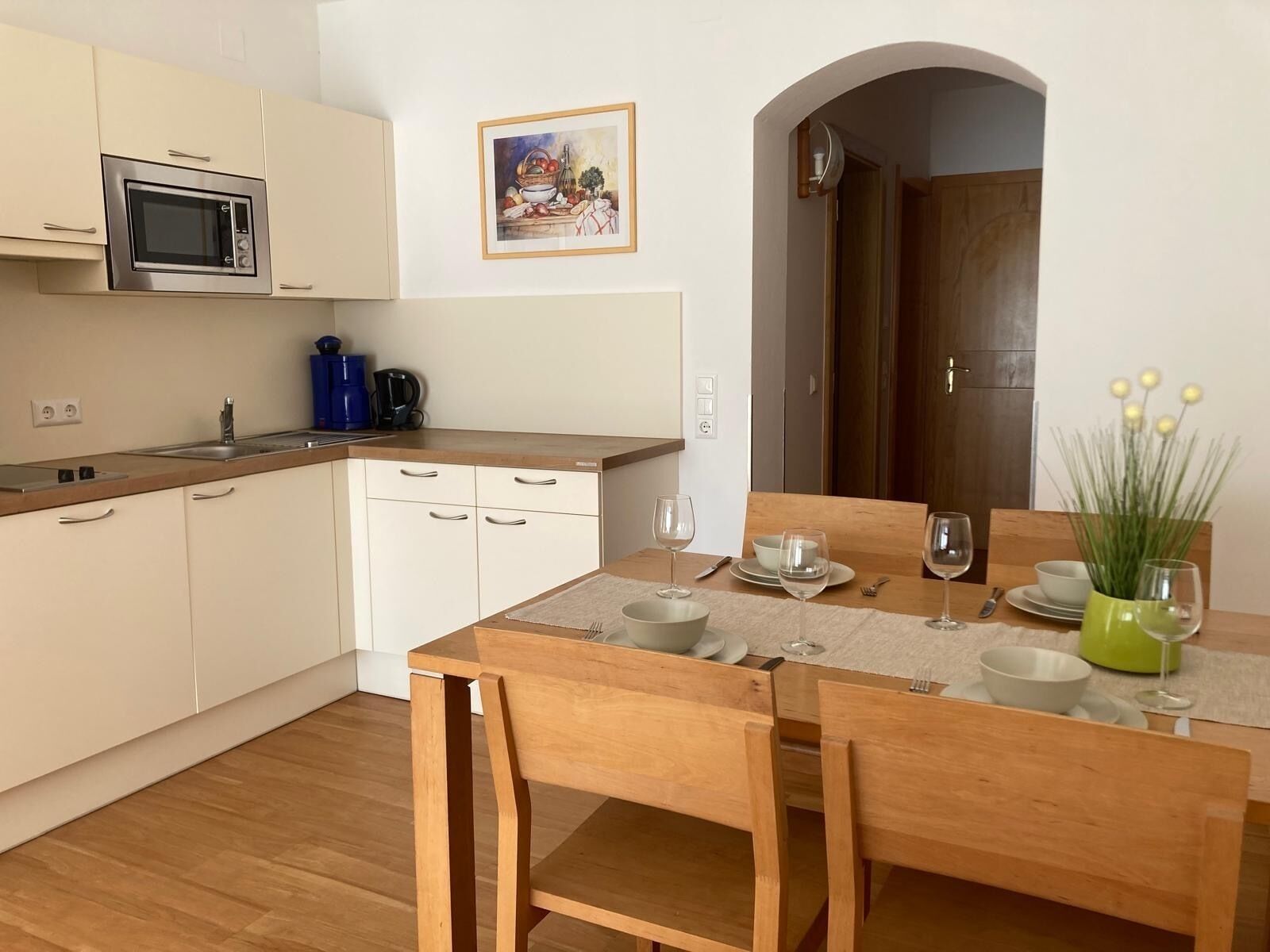 A modern kitchen with white cabinets, a built-in microwave, and a dining area with a wooden table set for two.