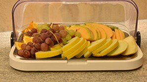 A food storage container with sliced apples, grapes, and orange segments. - Hotel Torwirt (Wolfsberg)