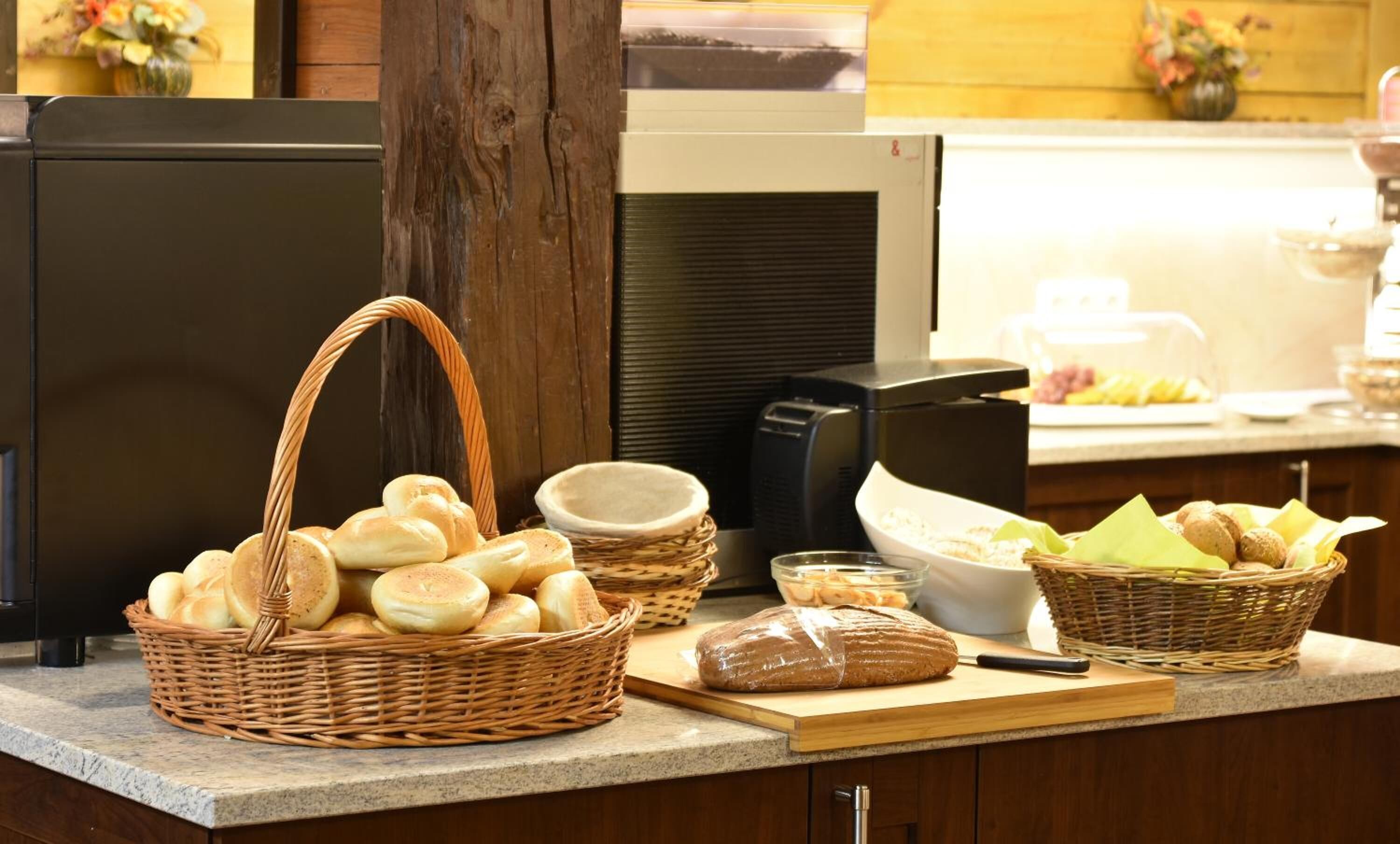 A buffet counter with baskets of bread, a cutting board, and a toaster.