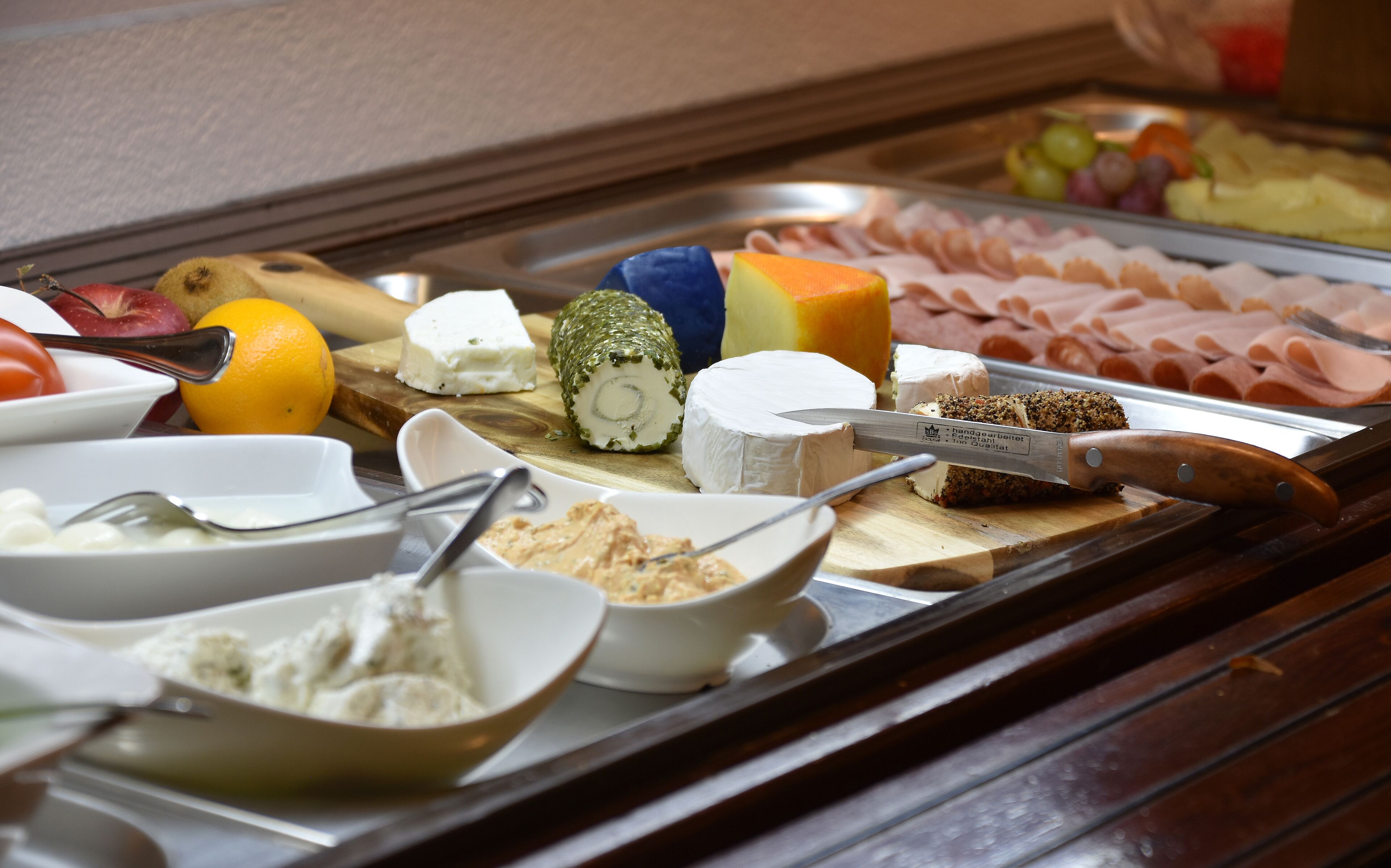 A buffet with various cheeses, fruits, and meats.