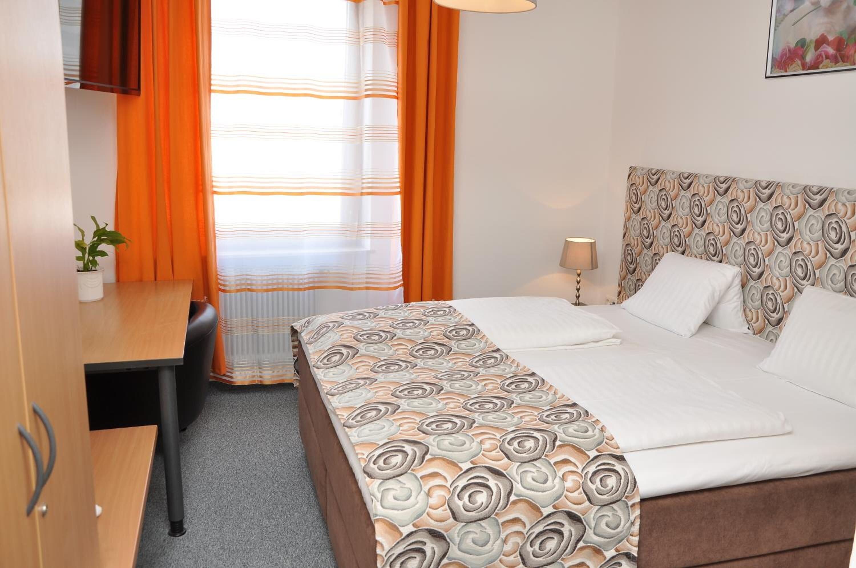 Een hotelkamer met een bed, een bureau, een stoel, een lamp en een potplant.