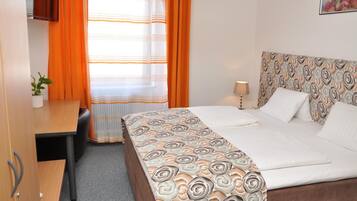 Een hotelkamer met een bed, een bureau, een stoel, een lamp en een potplant.