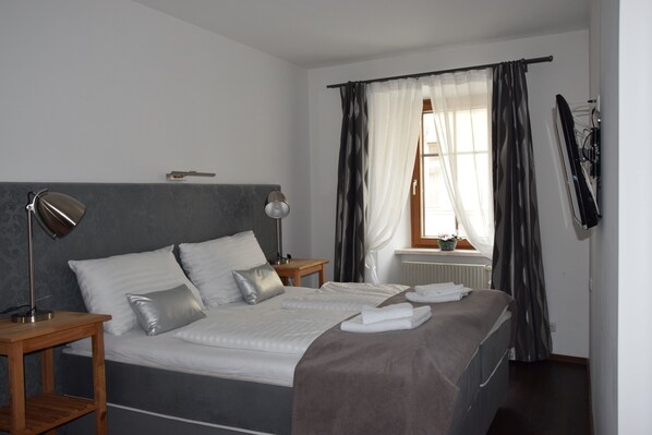 A neatly made bed with pillows and a blanket, a bedside table with a lamp, and a window with curtains. - Hotel Torwirt (Wolfsberg)